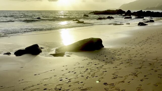 Panning shot of human footprints on golden sand leading to tropical sunset ocean