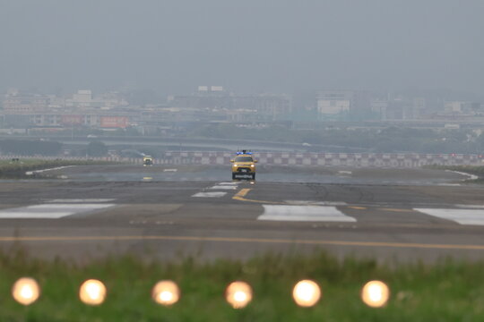 A yellow airport service vehicle drives on a foggy runway.