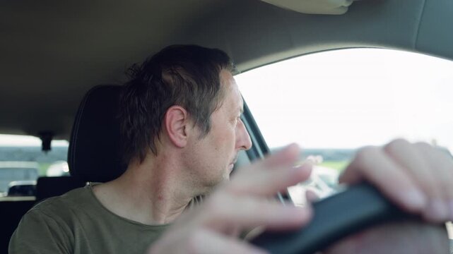 Middle-aged man waiting in car tapping steering wheel and looking out the window, impatient traffic moment, 4K