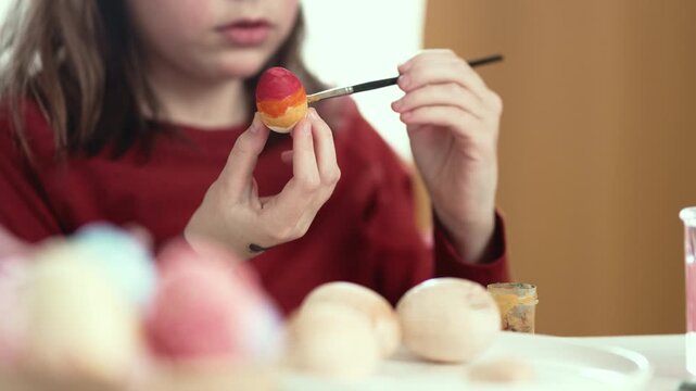 Little girl painting Easter eggs at home, 4K 10-bit cinematic footage of child decorating colorful eggs with watercolor brush for spring holiday, authentic lifestyle.