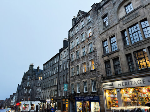 Evening street scene in historic Old Town Edinburgh Scotland UK with stone tenement buildings, illuminated shopfronts and wet pavement capturing traditional architecture and tourism atmosphere