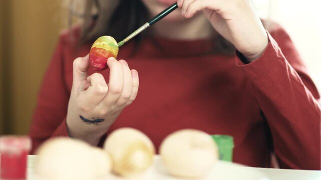 Little girl painting Easter eggs at home, 4K 10-bit cinematic footage of child decorating colorful eggs with watercolor brush for spring holiday, authentic lifestyle.