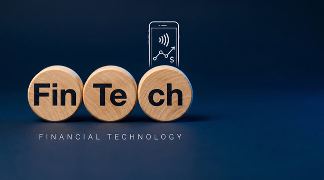 Three natural wood discs spelling FinTech with a smartphone payment and graph icon above on a deep midnight-blue background for financial tech.