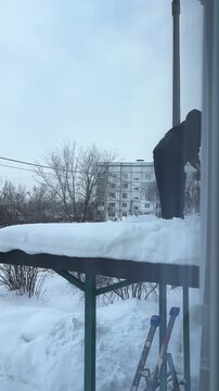 worker removing snow from the roof of an apartment building with shovel. unrecognizable person. vertical video