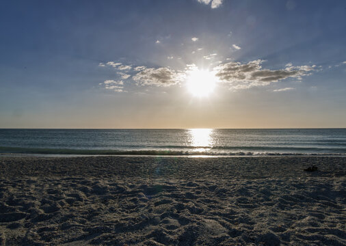 

Sunlight over a calm ocean and sandy beach with scattered clouds