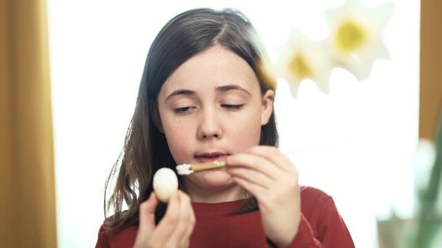 Little girl painting Easter eggs at home, 4K 10-bit cinematic footage of child decorating colorful eggs with watercolor brush for spring holiday, authentic lifestyle.