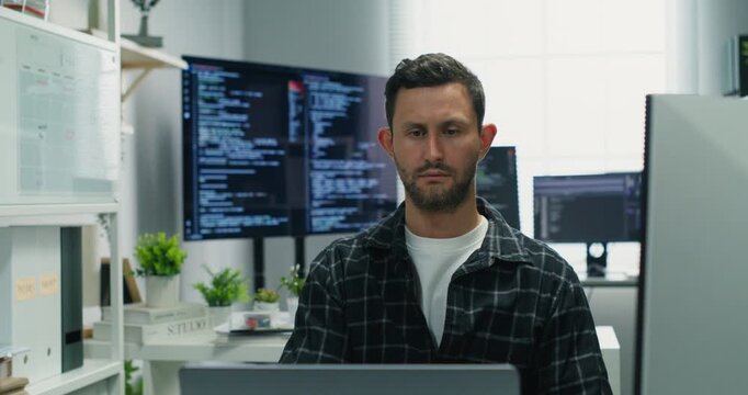  Caucasian man deep in thought at desk, planning secure network system architecture, coding, database analysis, AI integration and cybersecurity in a professional daytime office.