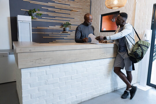 Assisting staff and gym member wearing sportswear signing forms at lobby desk, duffel, copy space