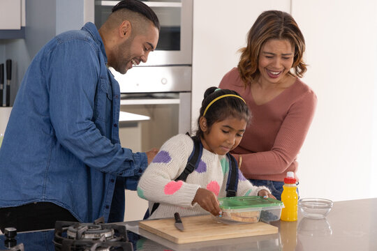 Diverse family adjusting backpack while closing green-lidded lunch container on kitchen island