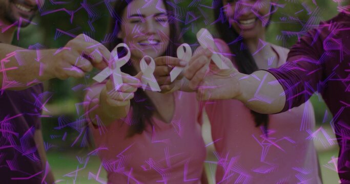 Holding pale pink ribbons, four adults in park wearing pink maroon tops with purple overlay