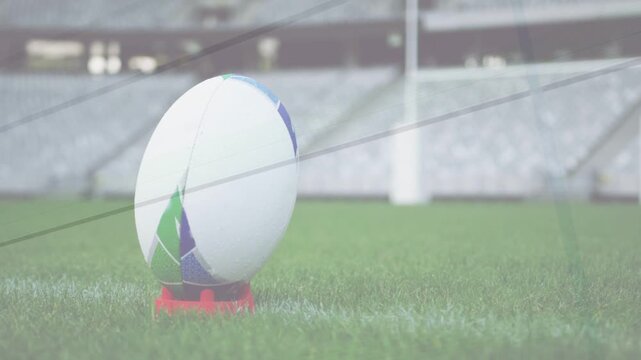 White rugby ball on red tee sitting on pitch, camera shifting, ropes crossing, preparing kick