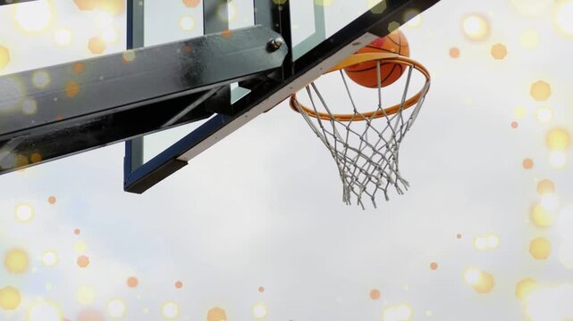 Player's arm lifting orange ball to rim, guiding entry, net stretching bokeh framing sports scoring