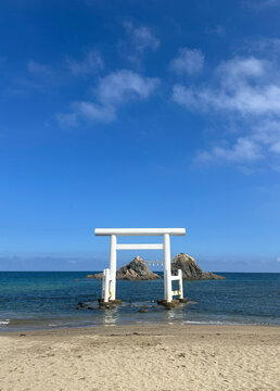 White torii gate standing in the sea with sacred rocks at Futamigaura beach in Itoshima