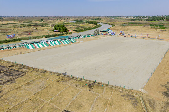 Aerial view of a vast, sandy arena bordered by a vibrant green and white grandstand, framed by the winding river and expansive landscape, Argungu, Kebbi, Nigeria.