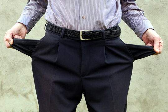 Businessman showing empty pockets standing against wall