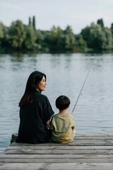 Fototapeta premium Woman and child sitting with fishing rod by lake on dock