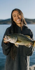 Fototapeta premium Young woman smiling while showing big fish at lake pier