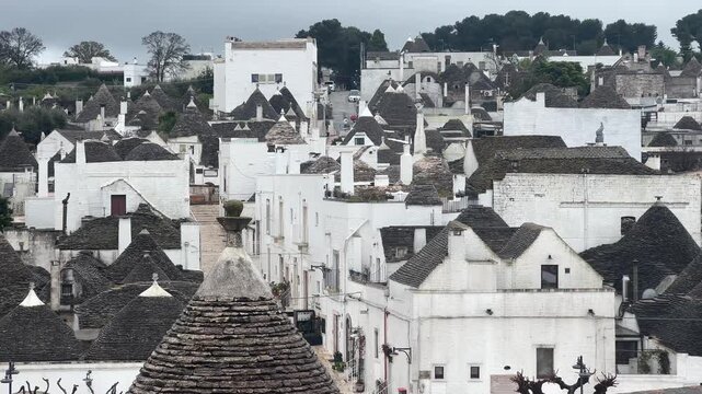 Panoramic view of traditional trulli houses in Alberobello, Italy, under a cloudy sky, showcasing unique historic architecture and European cultural heritage.