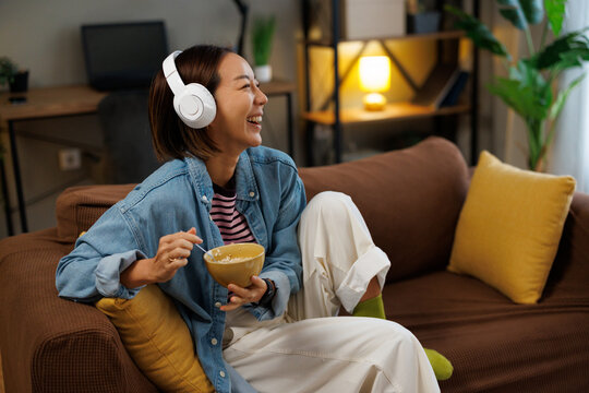 Young asian woman enjoying music and eating cereal and smiling