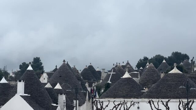 Panoramic view of traditional trulli houses in Alberobello, Italy, under a cloudy sky, showcasing unique historic architecture and European cultural heritage.