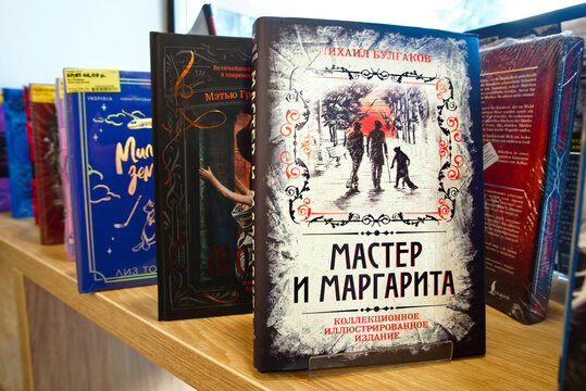 Minsk, Belarus. Apr 12, 2026. Master and Margarita by Mikhail Bulgakov on wooden bookstore shelf among other popular titles and modern literary fiction novels. Russian literature on bookstore shelf
