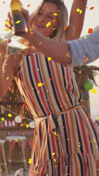 Vertical video: Woman taking handed bottle and dancing at bar, confetti floating around her for ads