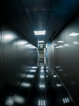 金属パネルの壁面と天井の照明が反射する近未来的なオフィスビルの無機質な通路
