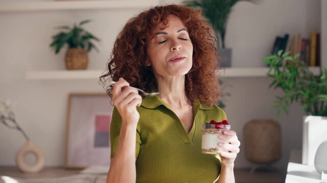 Video of  beautiful mature woman eating a yogurt with oats and red berries in the living room at home