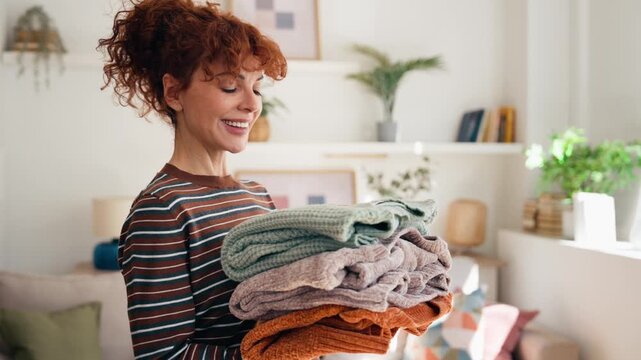 Video of beautiful mature woman holding clean clothes at home.