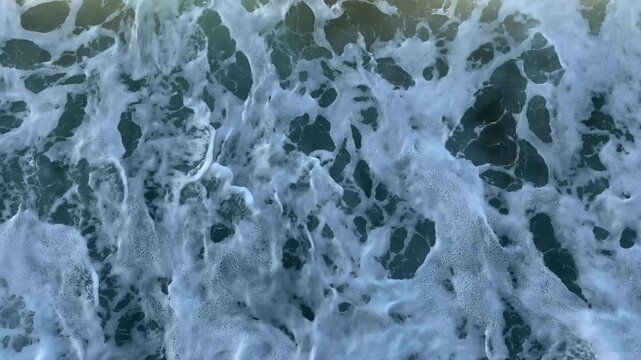 4K aerial close-up of white ocean foam churning on dark teal water. Fully abstract natural texture filling the entire frame. Ideal for seamless loop backgrounds, motion graphics, and wellness content