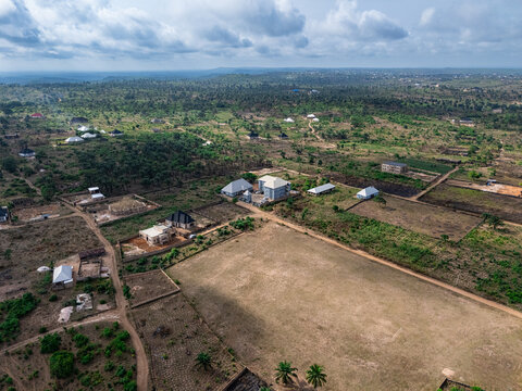 Aerial view of a sprawling rural landscape with scattered buildings, a vast sun-drenched field, and lush green vegetation under a cloudy sky, Elu, Abia, Nigeria.