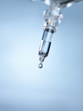 A close-up of a clear IV fluid drip chamber with a droplet forming at the tip.