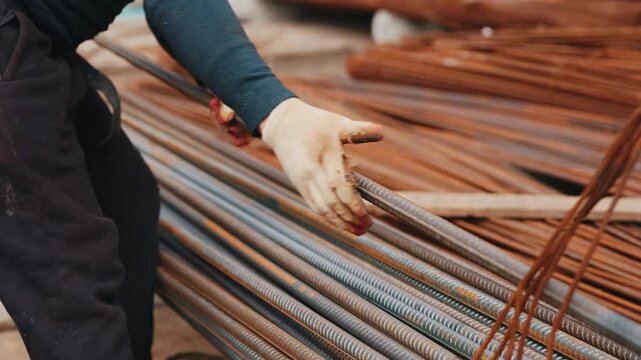 Worker repositioning steel rebar rods in stack at construction site