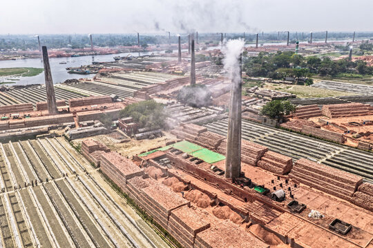 Aerial view of towering smokestacks spewing plumes over countless reddish-brown brick kilns along the Buriganga River, Narayanganj, Dhaka Division, Bangladesh.