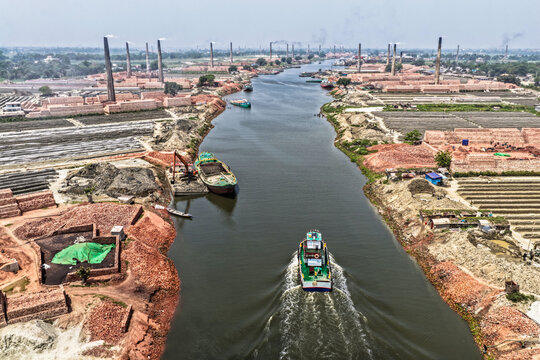 Aerial view of the dark Buriganga River winding through a landscape dominated by countless red brick factories with tall chimneys, Narayanganj, Dhaka Division, Bangladesh.