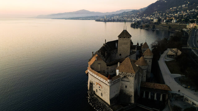 Aerial view of the stoic Chillon Castle standing firm against the tranquil waters of Lake Geneva, a timeless sentinel against the fading light, Veytaux, Vaud, Switzerland.
