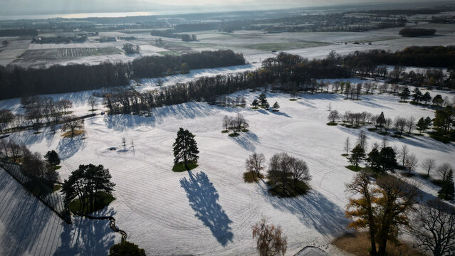 Aerial view of sun-drenched snow casting long shadows across the golf course near 31 Route de Bonmont, Cheserex, Vaud, Switzerland.