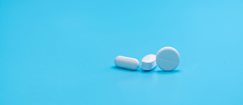 Round white tablets pills and oval tablets pills on blue background. Pharmacy shop banner. Prescription drugs. Pharmaceutical industry. Painkiller, antibiotics, and antacid tablet pills. Pharmaceutic.