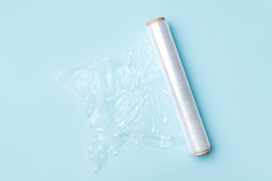 Roll of transparent food wrap for packaging and storing food products on blue background. Kitchen packaging materials, flat lay top view