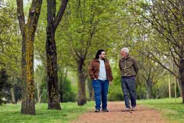 Fototapeta premium Intergenerational Conversation: Older Man and Younger Man Walking Together in Spring Park Path