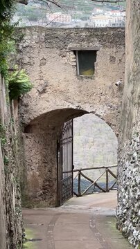 Narrow stone passage with an ancient archway and iron gate at Villa Cimbrone in Ravello, Italy, overlooking a scenic hillside landscape.