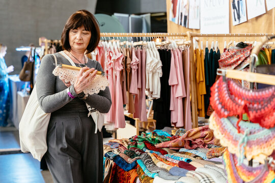 Caucasian mature woman checking handmade textile at indoor craft market