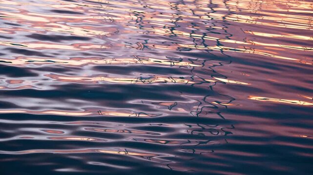 Gentle ripples move across marina water in Cannes, France, near the Palais des Festivals and the Carlton Hotel, bending mast reflections in warm sunset light.