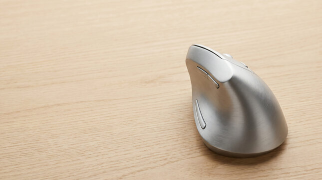 Modern Silver Vertical Ergonomic Mouse on a Minimalist Light Wood Desk Surface, High-Tech Computer Peripheral for Carpal Tunnel Prevention and Healthy Hand Posture in Professional Home Office Setups