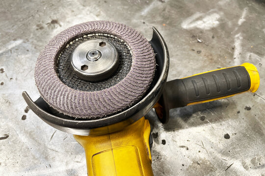 Yellow angle grinder with abrasive flap disc on metal table. Power tool workshop concept. Industrial cutting equipment background. Construction repair scene. Hardware machinery closeup view.