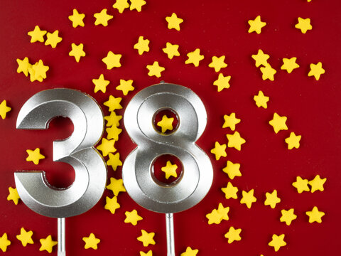 Concept of celebrating birthday and anniversary. Number 38 thirty eight silver celebration birthday candle on festive red Background. Thirty eight years birthday.