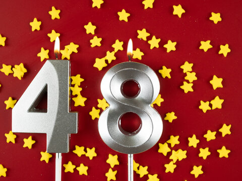 Concept of celebrating birthday and anniversary. Number 48 forty eight silver celebration birthday candle on festive red Background. Forty eight years birthday.