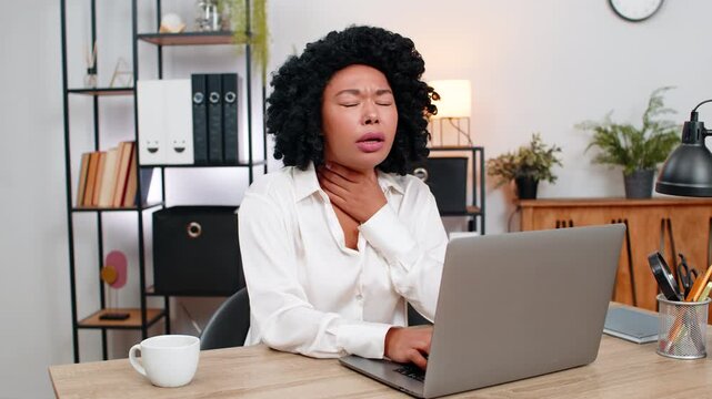 African American businesswoman at home office holds throat struggling to swallow enduring sharp pain looking sick. Freelancer girl at table feels weak plans doctor visit seeking urgent aid soon today.