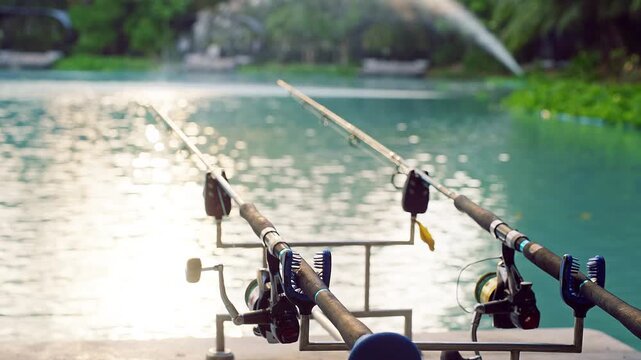 Fishing Rods Positioned over Calm Lake Water with Bright Sun Reflection Fountain in Background Leisure Activity Outdoor Recreation and Relaxation Scenic Environment