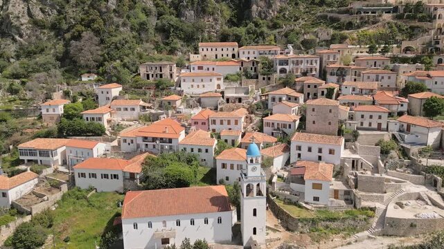 Aerial panoramic view historic hillside village of Dhermi in Albania. Traditional orange rooftop stone houses and iconic Holy Church of Saint Spyridon